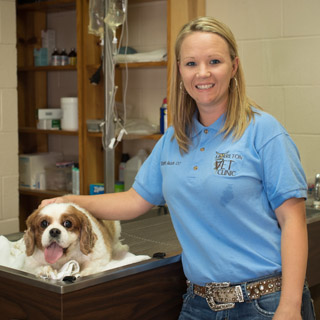 Stephanie Jackson, CVT standing and smiling next to a happy brown and white dog at Morrilton Veterinary Clinic in Morrilton, AR
