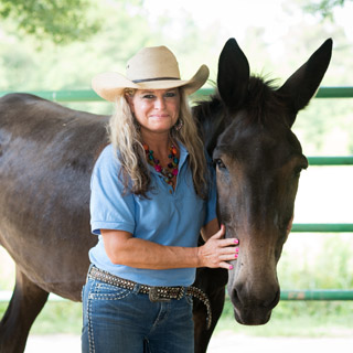Sheri Turner in a large straw hat standing next to and petting a large brown donkey at Morrilton Veterinary Clinic in Morrilton, AR